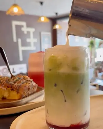 Matcha glacé vert pâle au-dessus d'une couche de purée de fraise, dans un verre