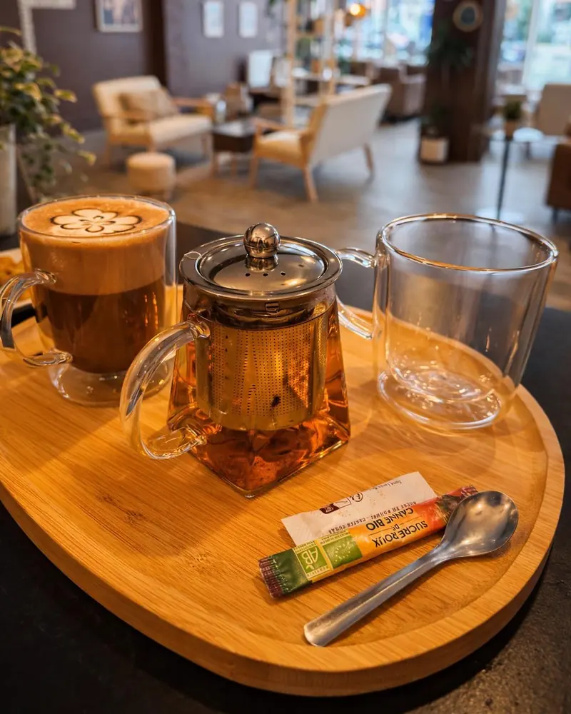 Plateau en bois avec une théière en verre, un latte et deux tasses, dans le salon